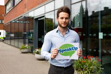Man holding a sign outside a hospital that says 'Speak Up'